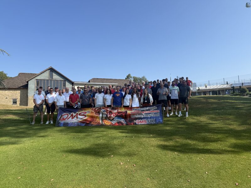 Fairway to Devon 2026 Golf Day participants and organisers at Dainton Golf Club in front of QMS banner