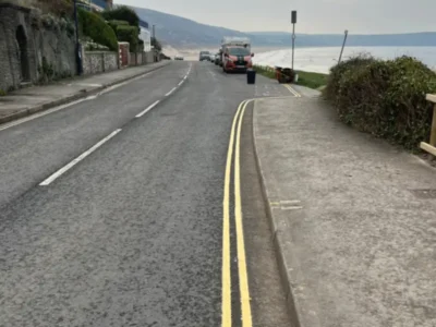 Freshly applied MMA double yellow lines along the kerb of a coastal road with a works van in the background